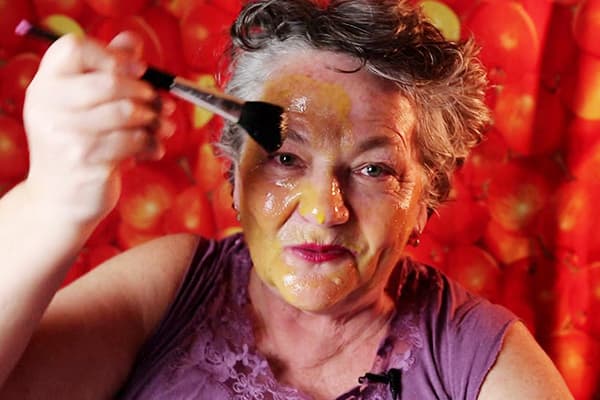 O femeie în vârstă își pune o mască de ou pe față